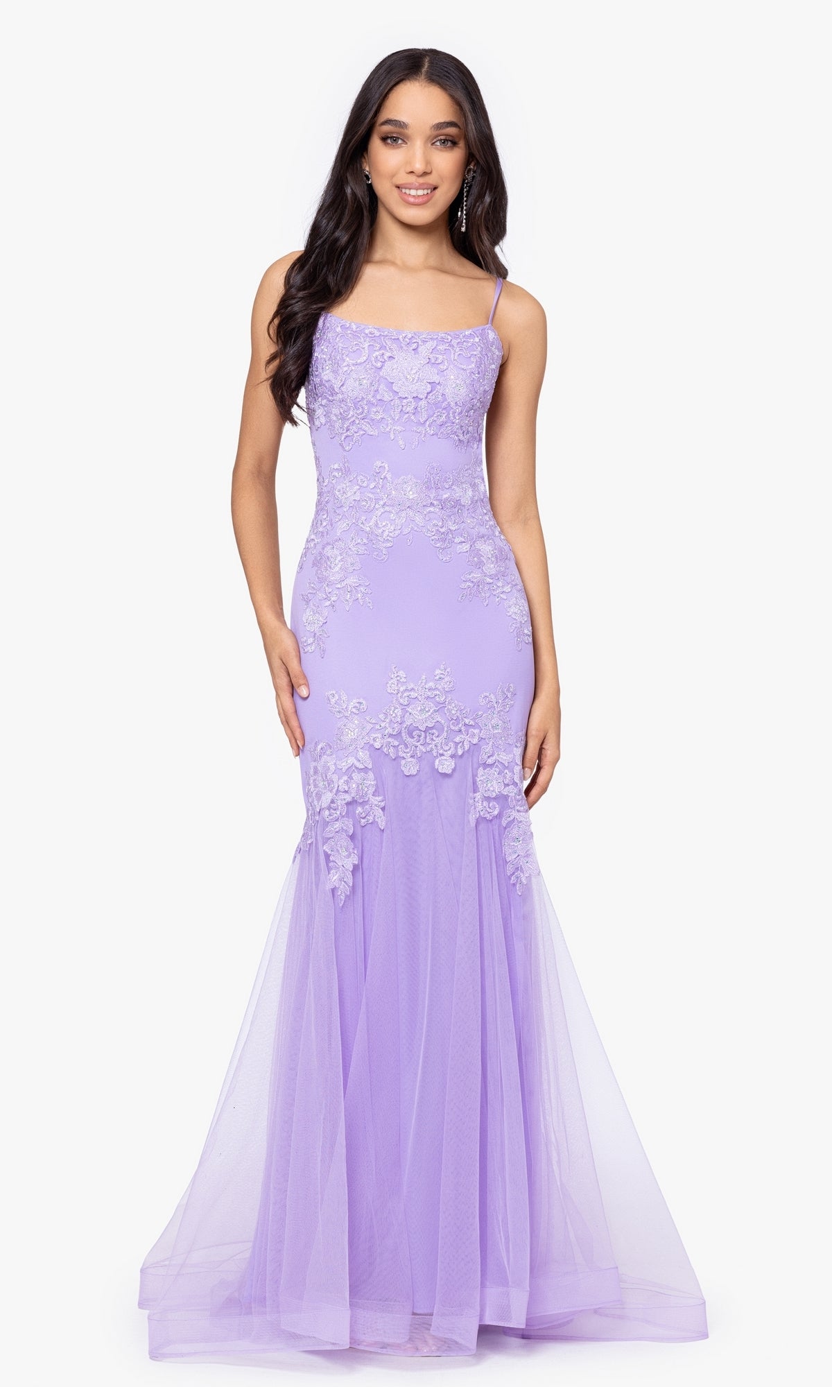 A woman in the Blondie Nites Lilac Purple Long Prom Dress 4706BN, featuring lace appliqué and thin straps, stands against a white backdrop.